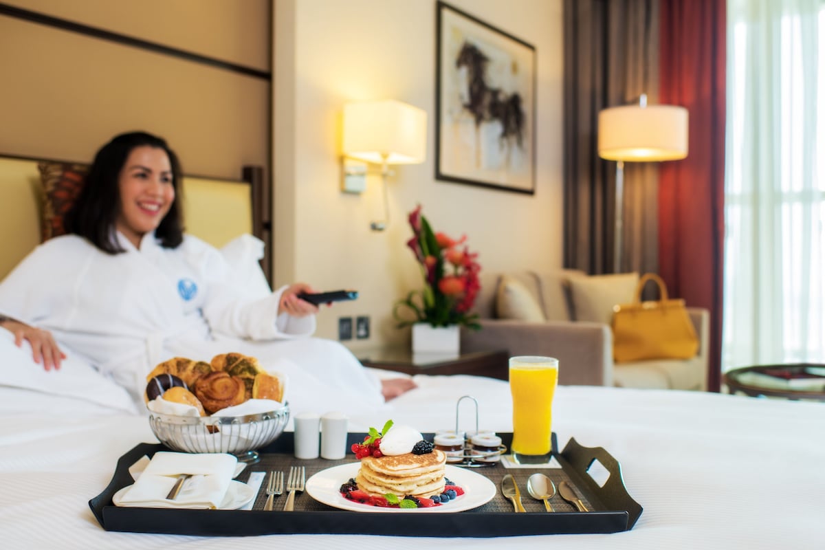 A hotel room with a breakfast tray on the bed, including pancakes, berries, and a glass of orange juice.