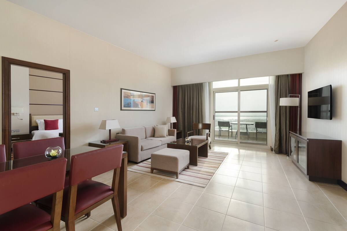 A hotel room with a dining area, a sofa, a TV, and a balcony with a view.