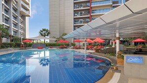 A swimming pool with red umbrellas, lounge chairs, and a pool bar named 'Aquarius'. - Park Rotana (Abu Dhabi)