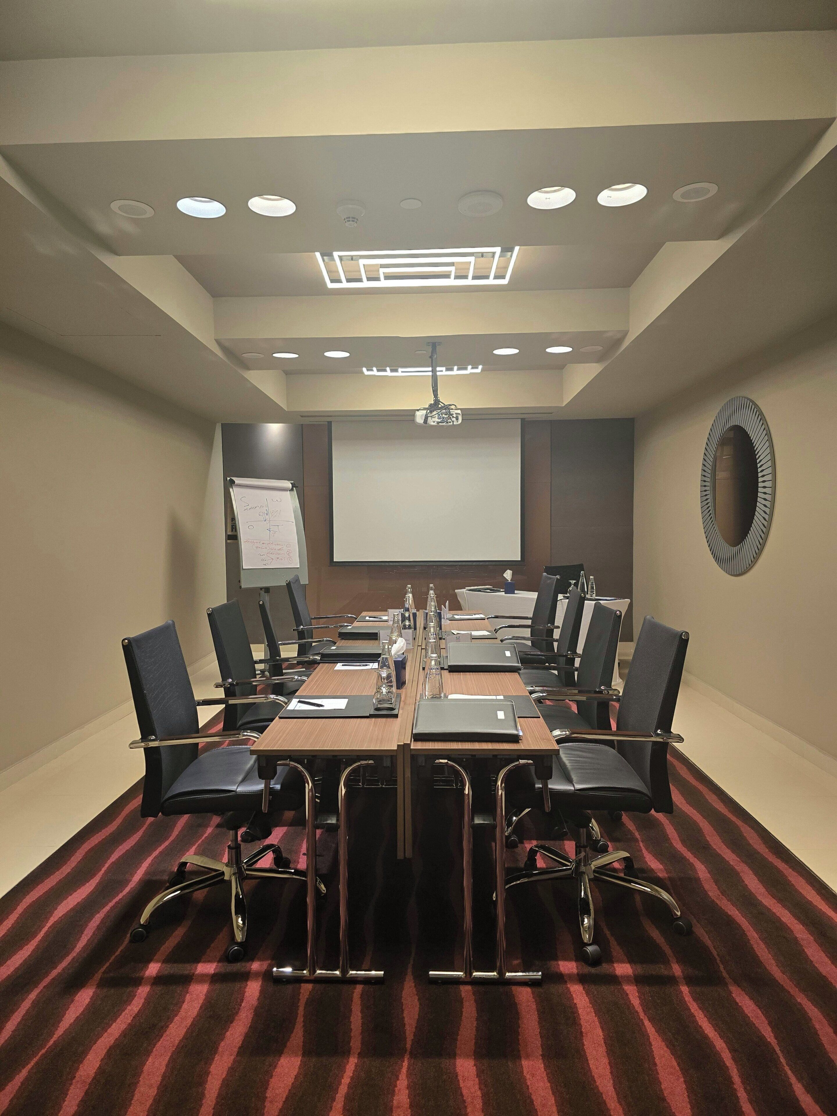Une salle de conférence équipée d’une longue table, de chaises, d’un écran de projection et d’un tableau blanc.