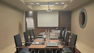Une salle de conférence équipée d’une longue table, de chaises, d’un écran de projection et d’un tableau blanc.