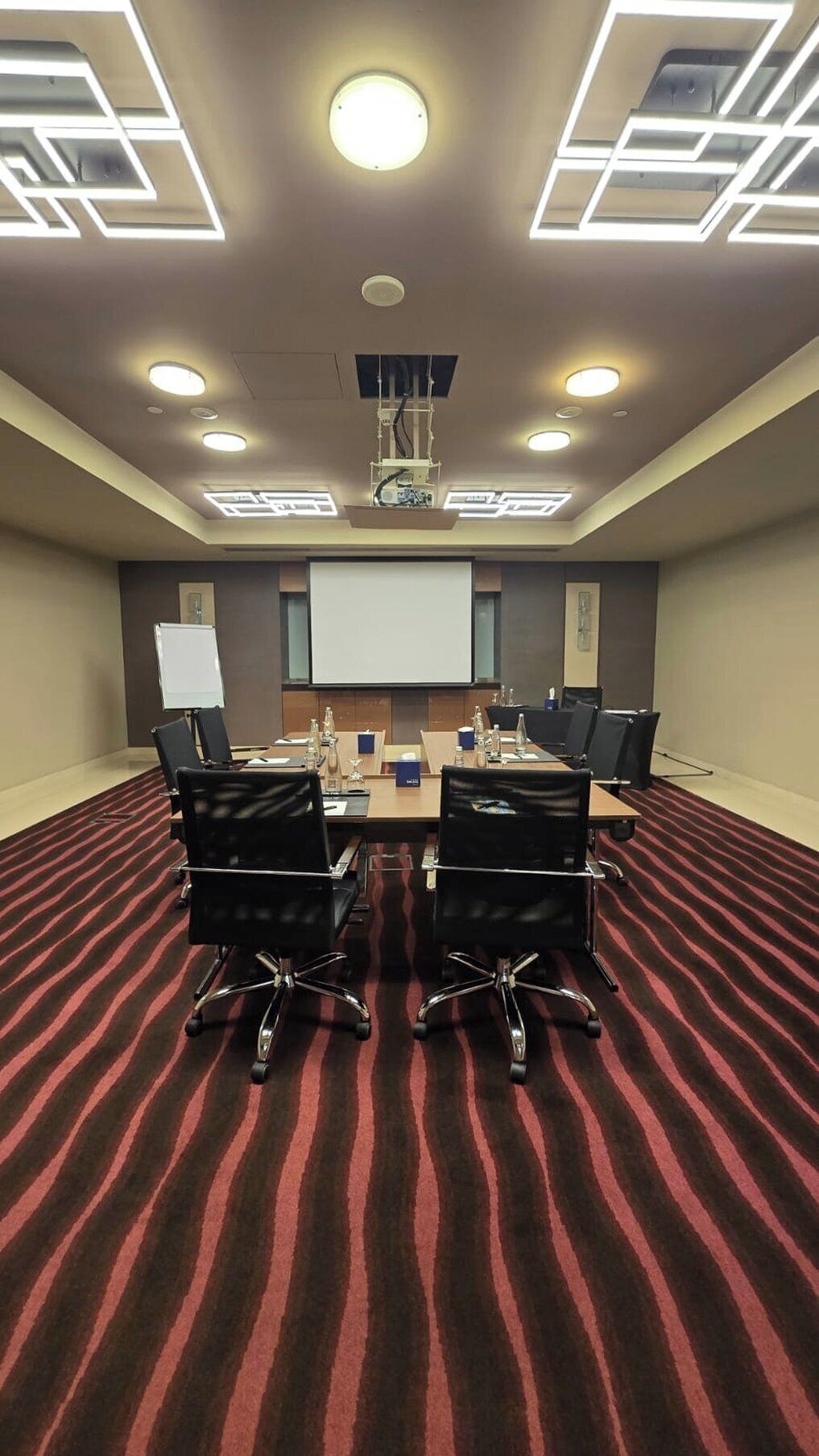A conference room with a red-striped carpet, a whiteboard, and a projector screen.