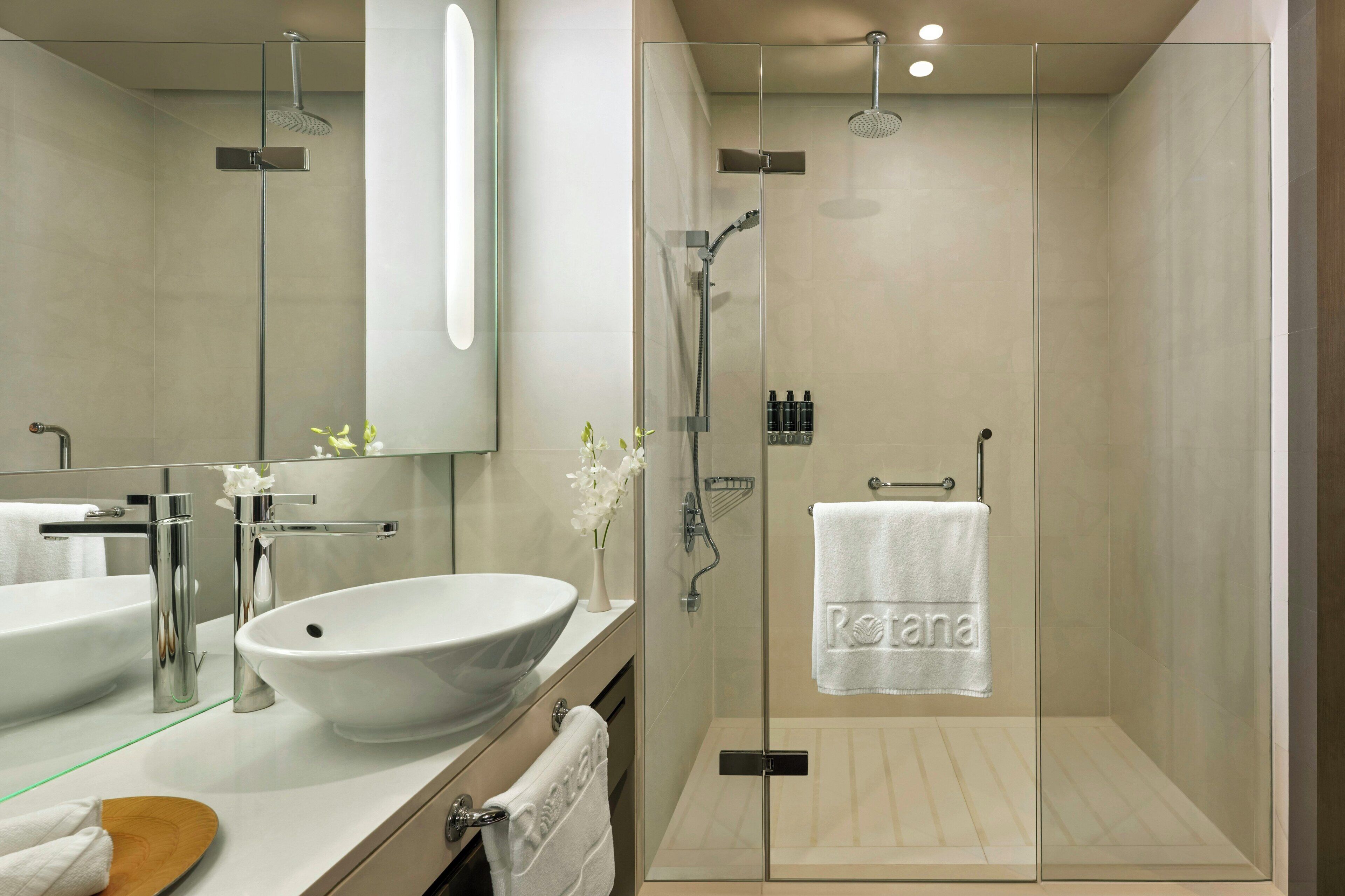 A modern bathroom with a glass-enclosed shower, a large white sink, and a mirror above the vanity.