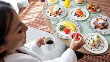A breakfast table with various dishes including pancakes, omelets, and pastries, and a person holding a cup.