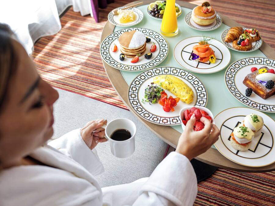 A breakfast table with various dishes including pancakes, omelets, and pastries, and a person holding a cup.