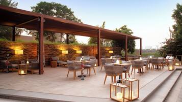Un patio al aire libre con varias áreas de estar, incluyendo sofás y sillones, bajo una pérgola de madera.