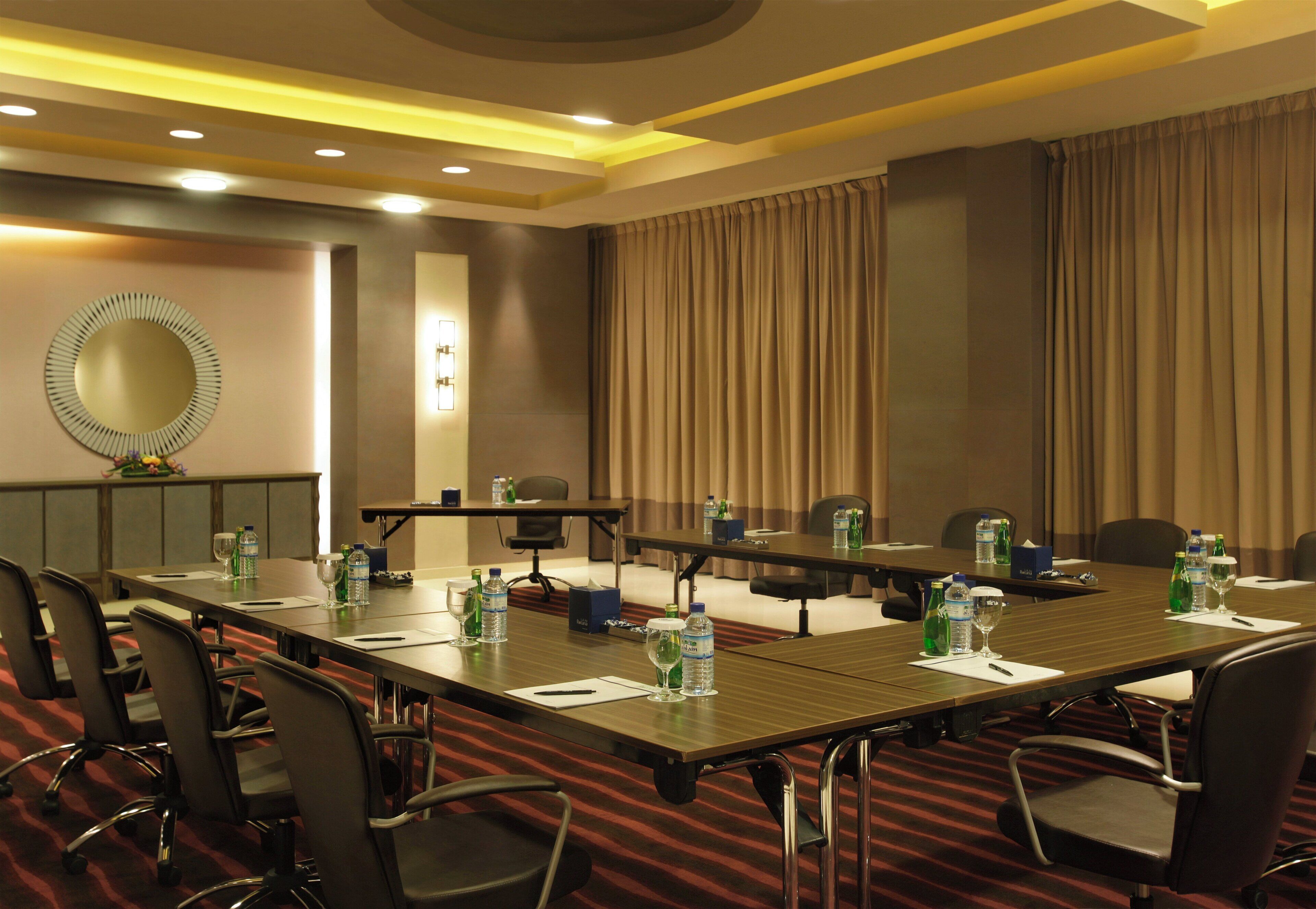 A conference room with a long table, chairs, water bottles, and a mirror on the wall.