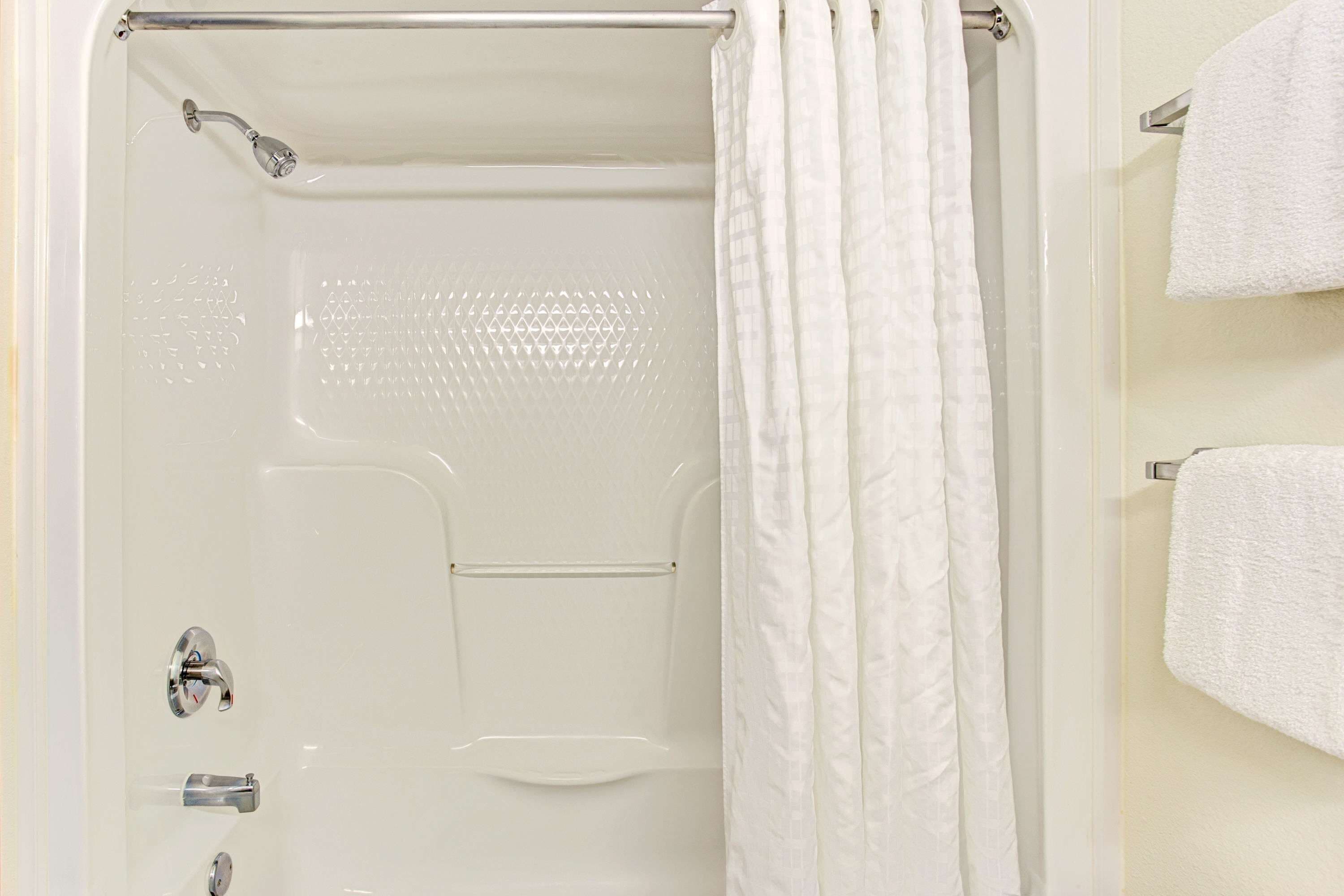 Ducha blanca con puerta de vidrio, cabezal de ducha y toallero con una toalla.