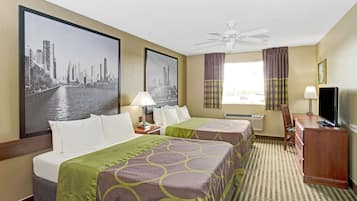 A hotel room with two beds, a desk, a TV, a ceiling fan, and large cityscape pictures on the walls.