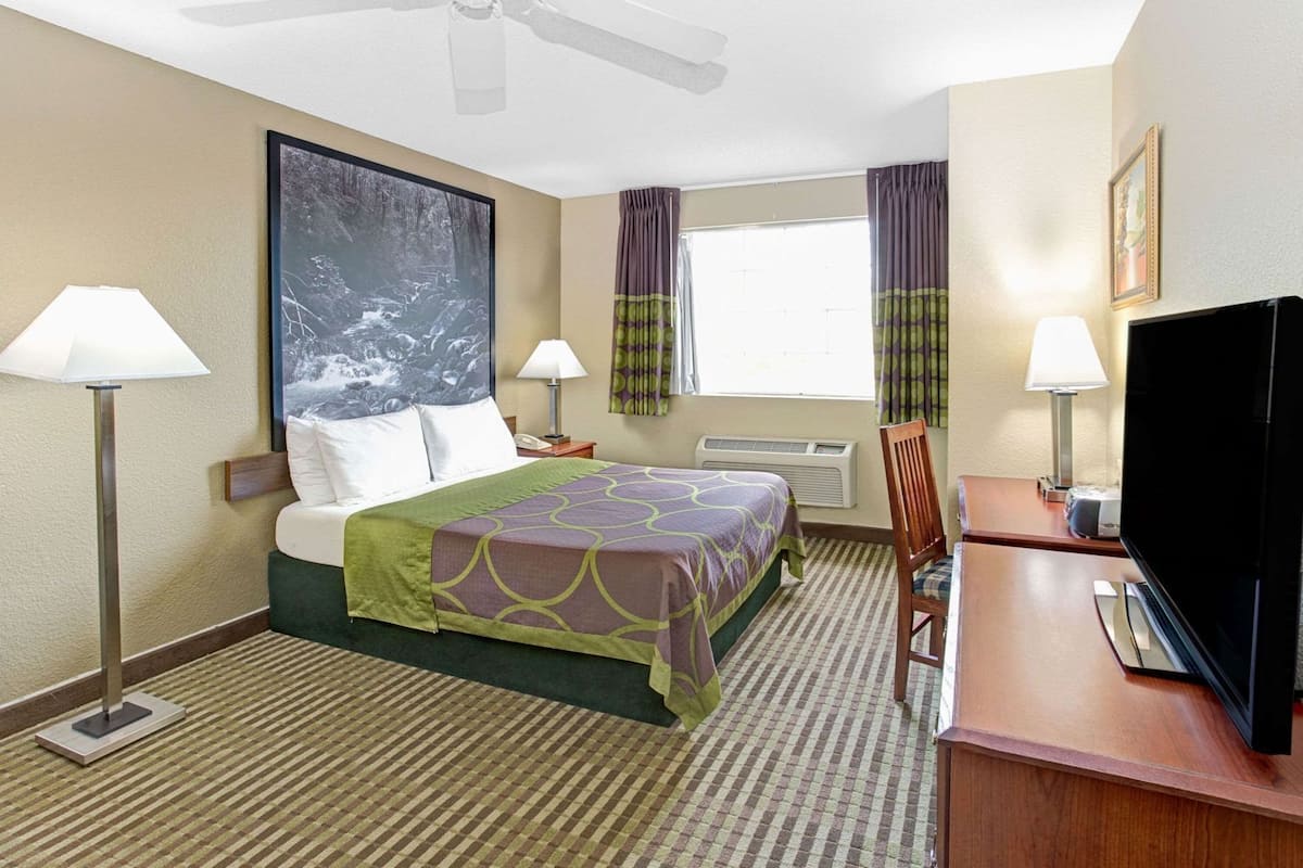 A hotel room with a bed, two bedside lamps, a flat-screen TV, a desk, and a chair.