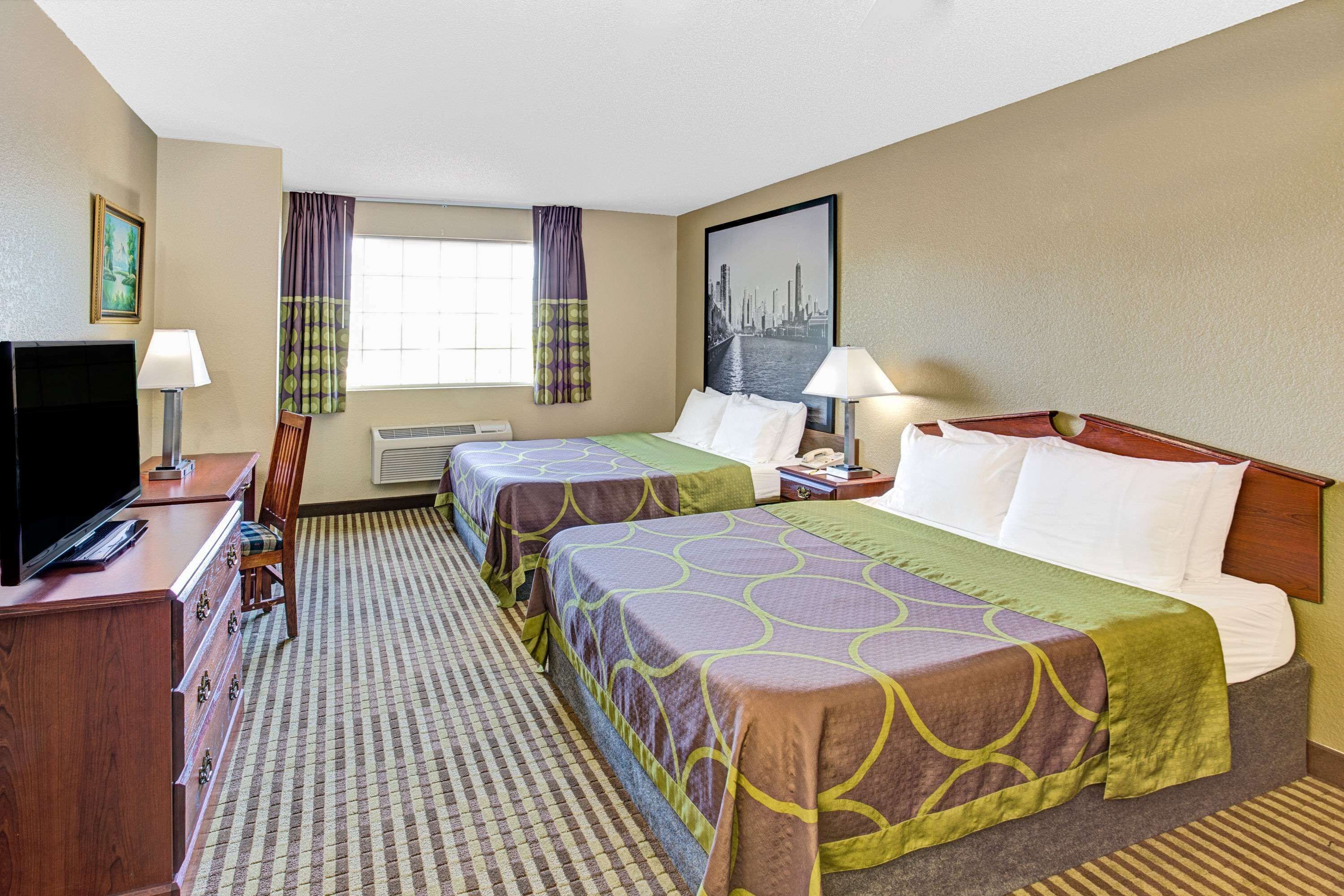 A hotel room with two beds, a TV, a desk, and a window with curtains.