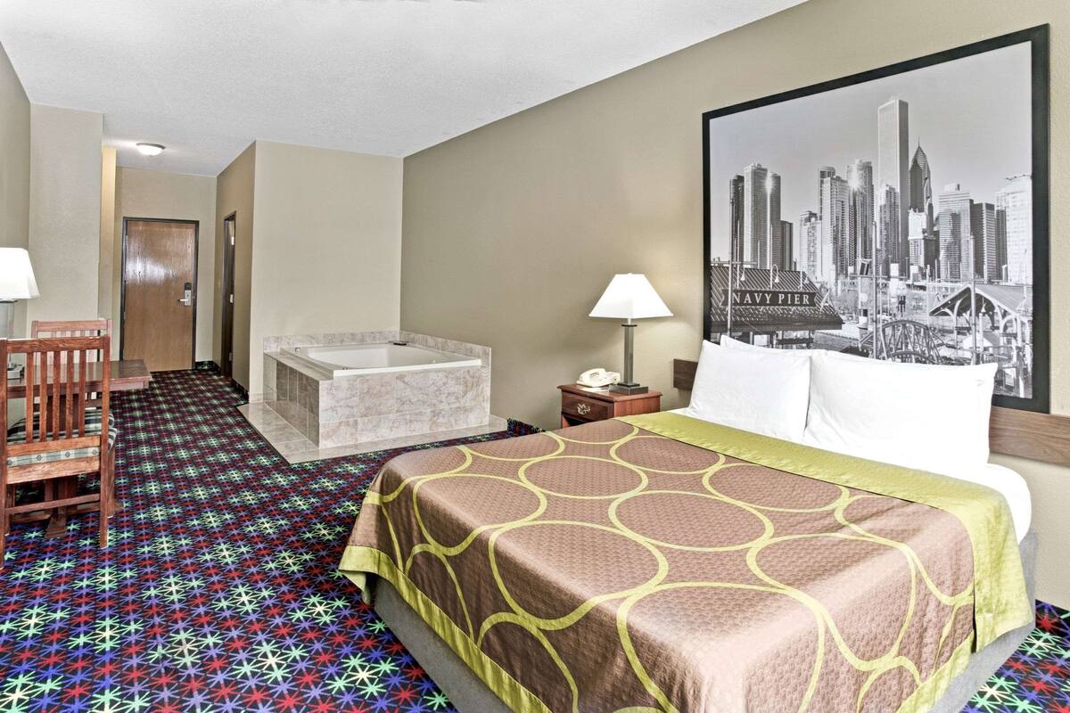 A hotel room with a bed, a desk, a chair, a bathroom, and a cityscape painting on the wall.