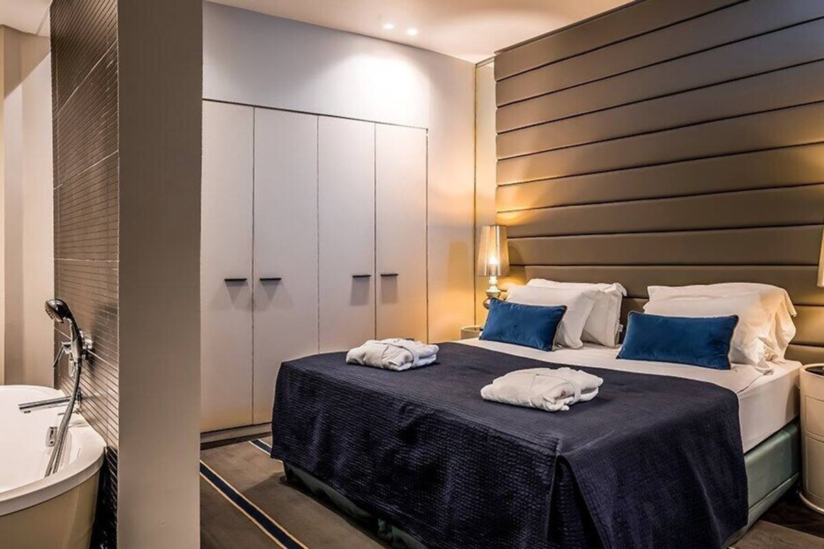 Una habitación de hotel moderna con una cama grande, baño privado y una mesita de noche con lámpara.