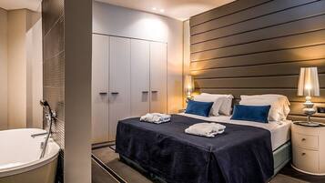 Una habitación de hotel moderna con una cama grande, baño privado y una mesita de noche con lámpara.