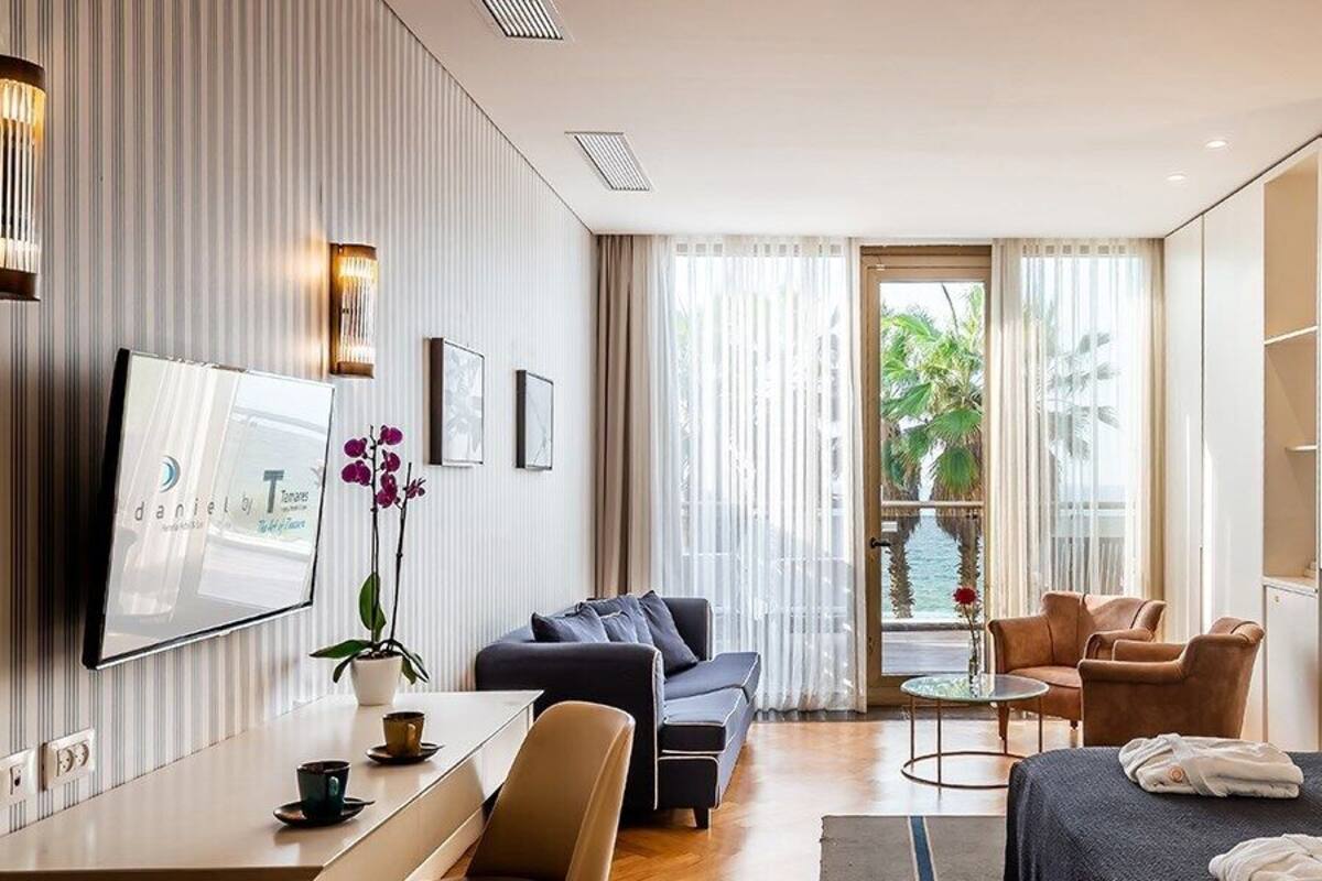 Una habitación de hotel moderna con cama, escritorio, sofá y balcón con vista a palmeras.