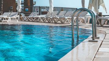 A swimming pool with clear blue water, surrounded by white lounge chairs and umbrellas.