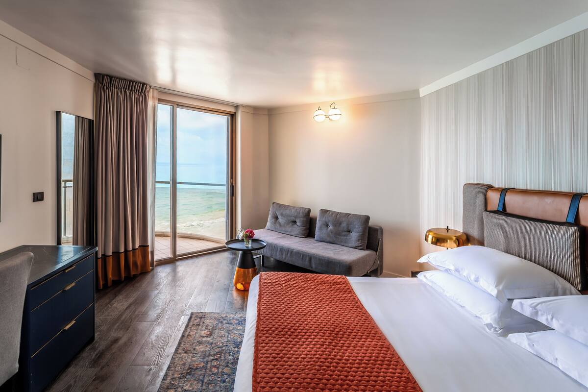 Habitación de hotel con cama, sofá, escritorio, televisor y vista al mar.