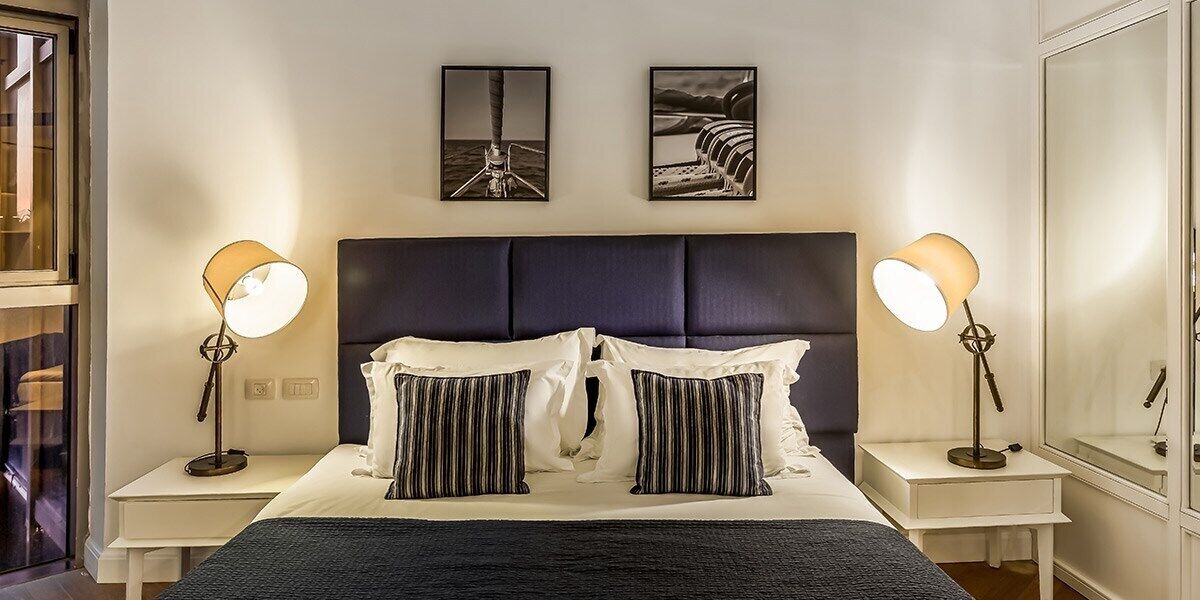 A modern hotel room with a large bed, two bedside tables, and two wall-mounted lamps.