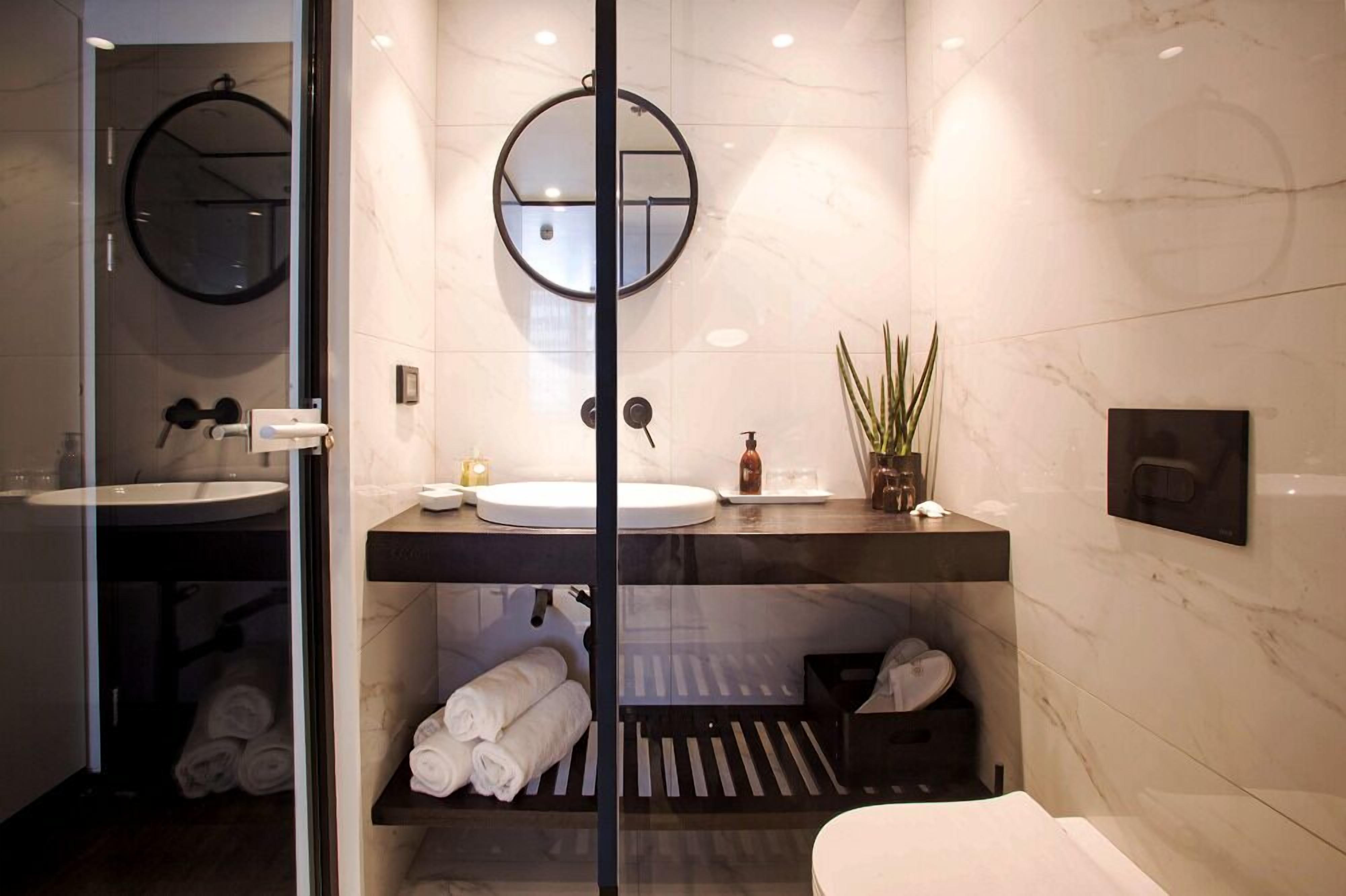 Un baño moderno con un espejo grande, dos lavamanos, un perchero para toallas y una planta pequeña.