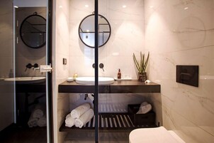 Un baño moderno con un espejo grande, dos lavamanos, un perchero para toallas y una planta pequeña.