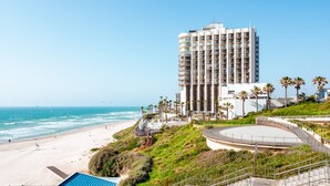 Un hotel frente a la playa con un edificio grande, una playa y palmeras.