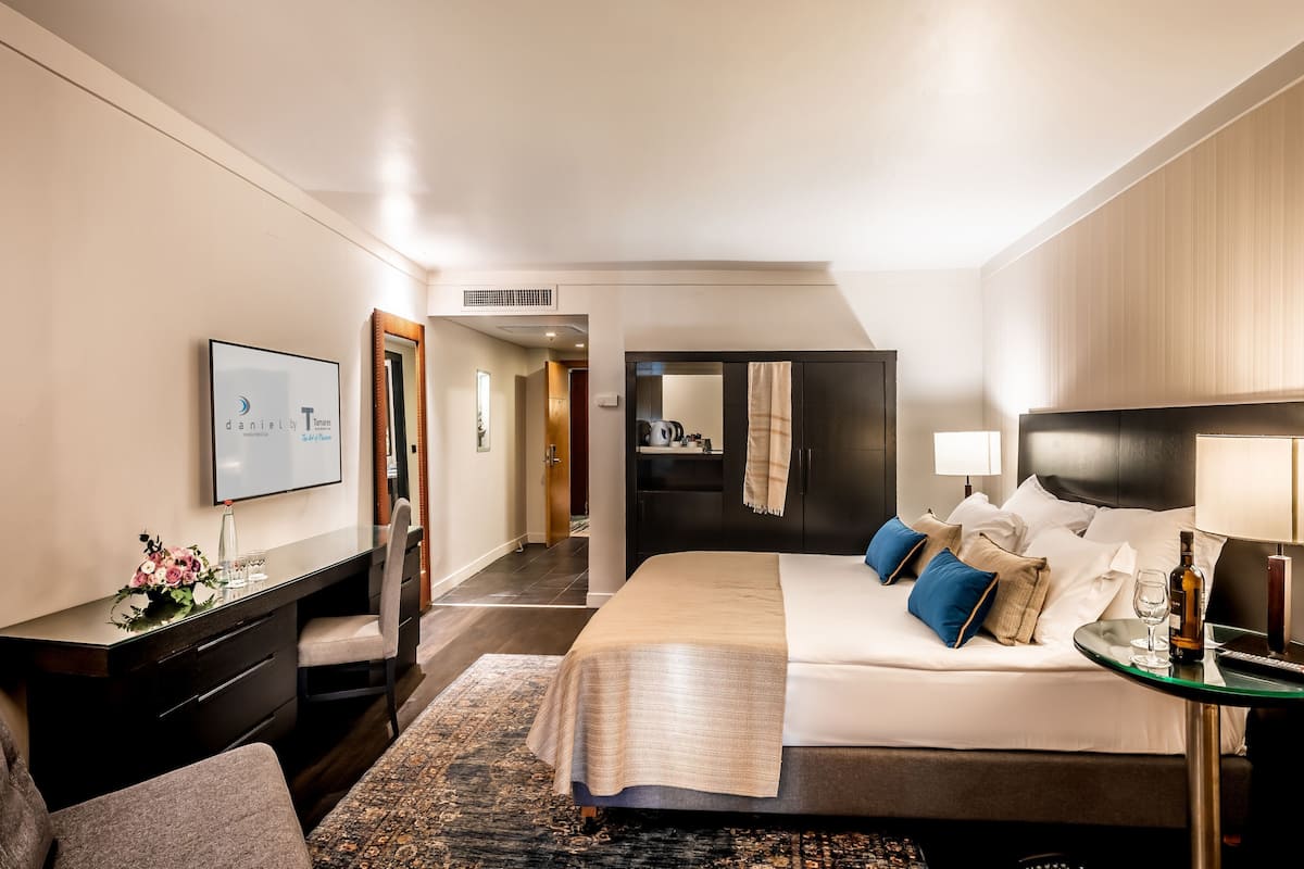 Una habitación de hotel con cama, mesita de noche, lámpara y televisor en la pared.