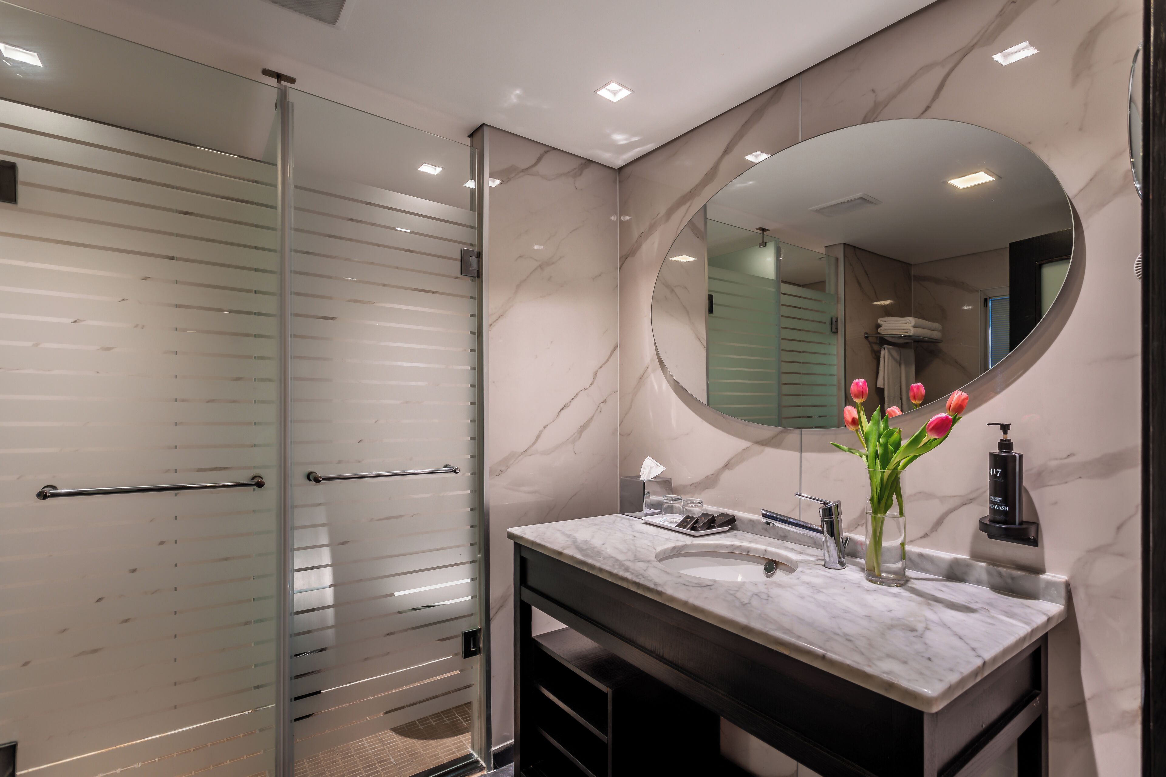 Un baño moderno con cabina de ducha de vidrio, lavamanos de mármol y un espejo grande.