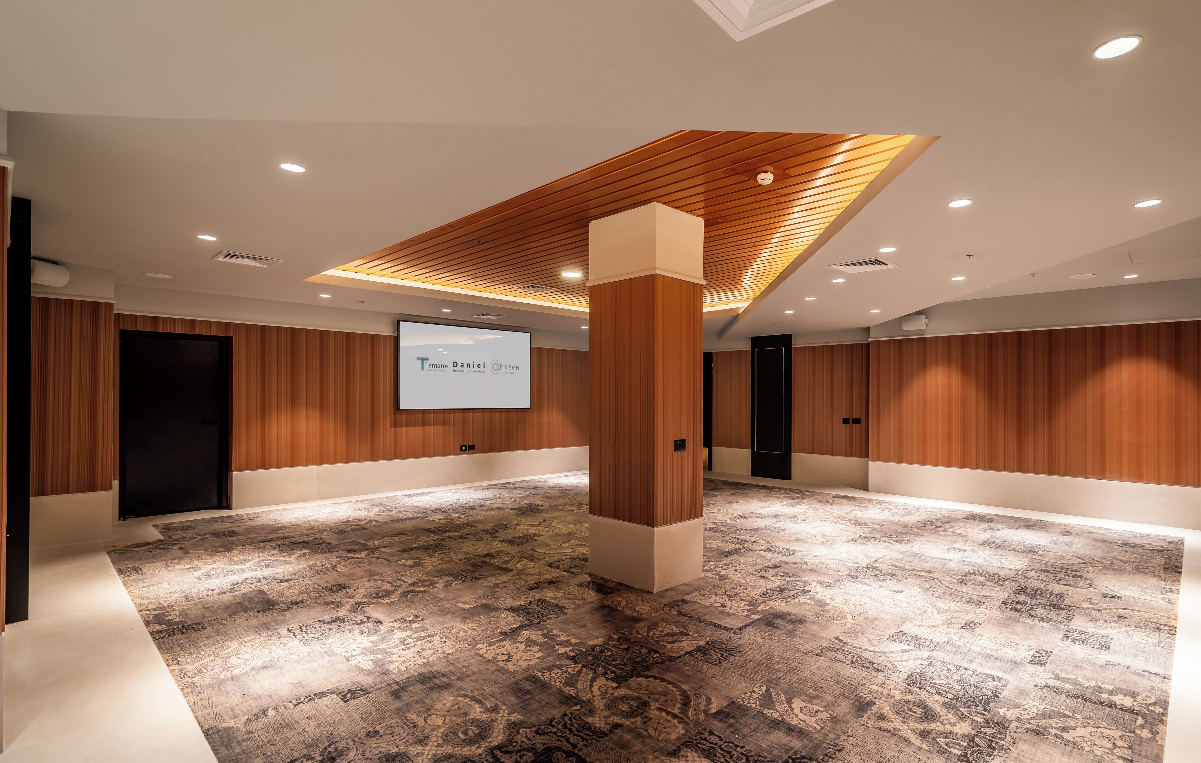 A conference room with a wooden panel ceiling, a large screen, and patterned carpet.