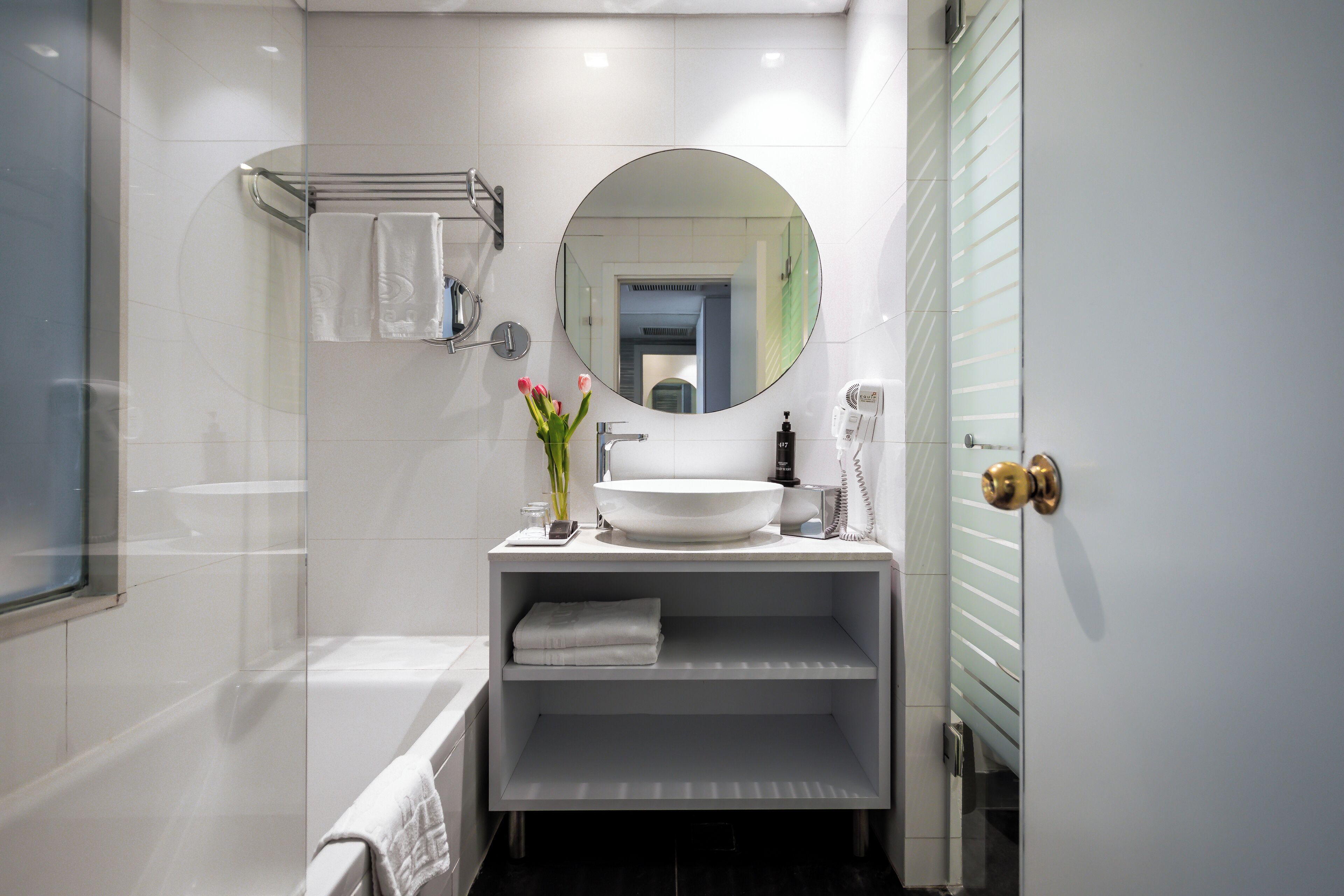 Un baño moderno con lavamanos, espejo y toallero blancos.