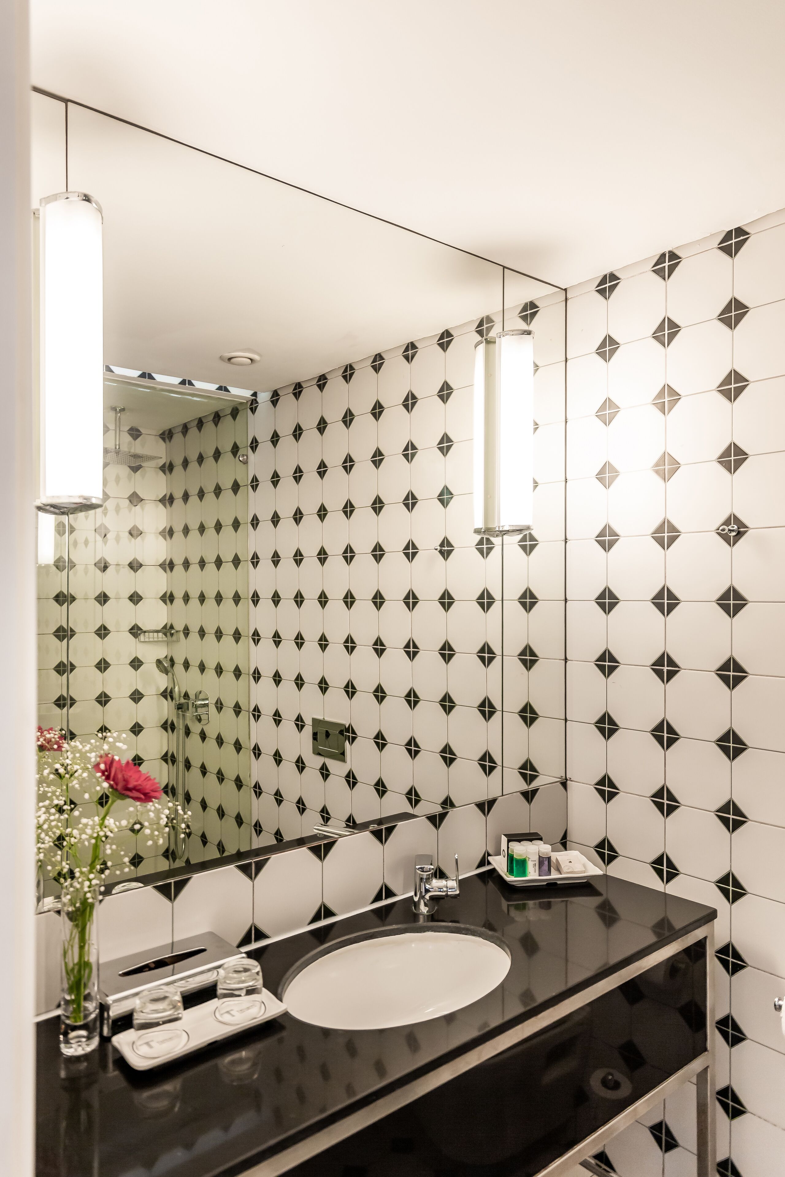 Un baño moderno con pared de azulejos blancos y negros, un espejo grande, encimera negra y lavamanos blanco.
