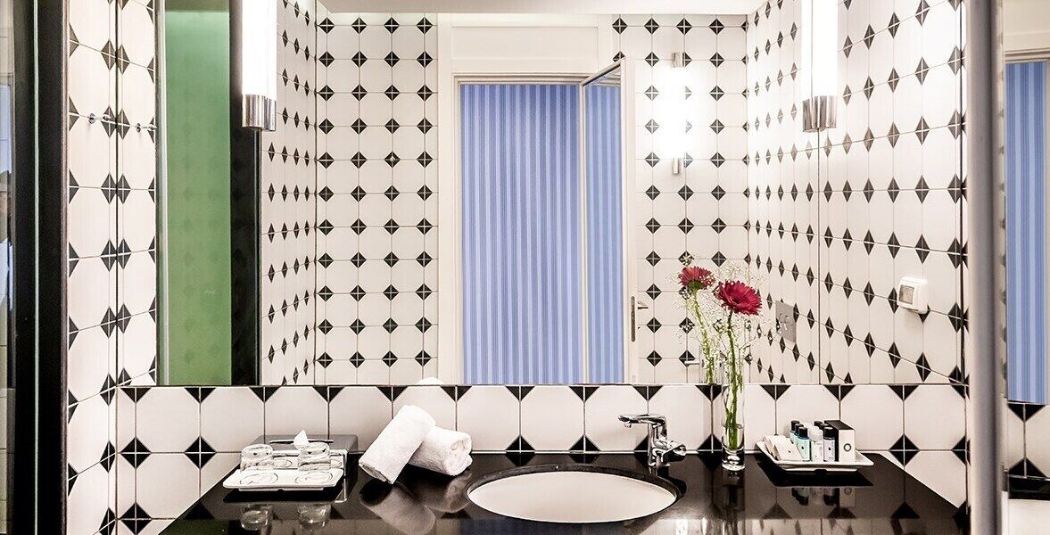 Une salle de bain avec un mur recouvert de carreaux noirs et blancs formant un motif, un rideau de douche bleu, un lavabo avec un miroir et un vase rempli de fleurs rouges.
