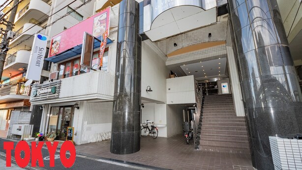 A hotel entrance with a modern design, featuring a staircase leading to the upper floors and a bike parked outside. - Sky Heart Hotel Koiwa (Tokyo)