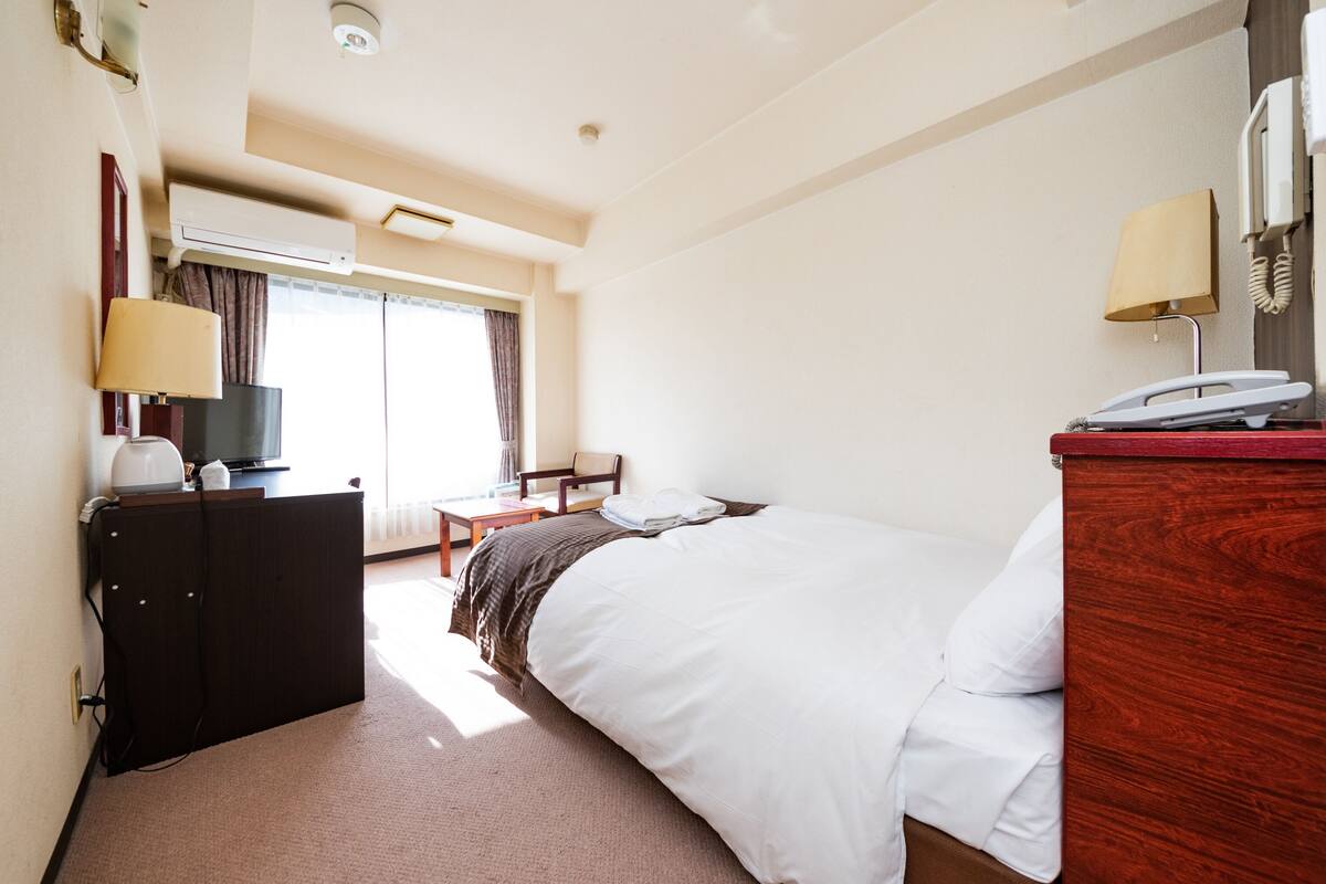 Une chambre d’hôtel équipée d’un lit, d’un bureau, d’une chaise, d’une commode, d’une lampe, d’un téléphone et d’un appareil de climatisation.