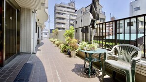 A narrow outdoor corridor with a tiled floor, a small table with chairs, and potted plants. - Sky Heart Hotel Koiwa (Tokyo)
