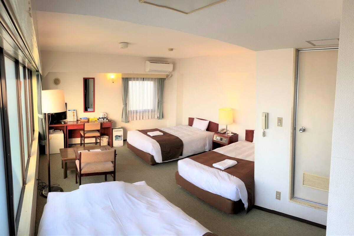 Une chambre d’hôtel avec deux lits, un bureau, une chaise et une fenêtre avec des rideaux.