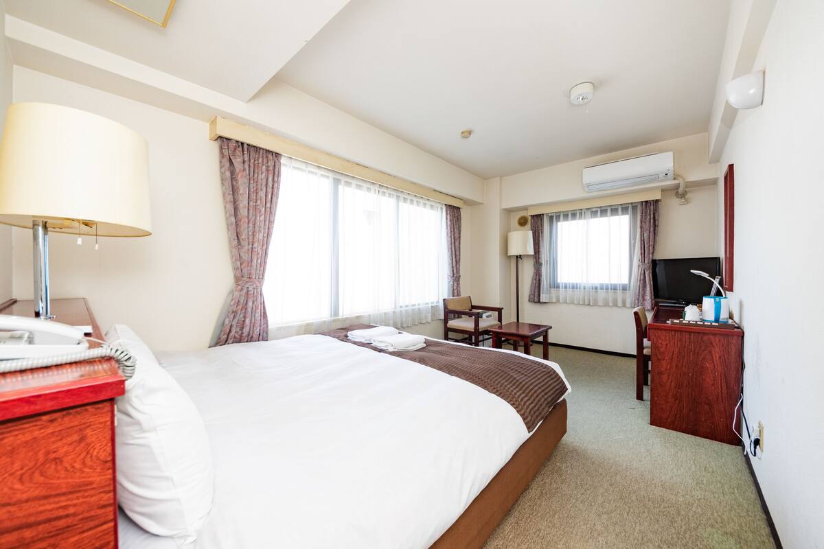 Une chambre d’hôtel avec un grand lit, un bureau, une chaise, une télévision et un appareil de climatisation.
