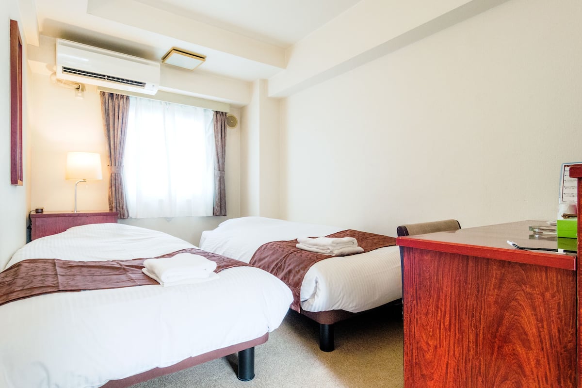 Une chambre d’hôtel avec deux lits, un bureau, un climatiseur et une fenêtre avec des rideaux.