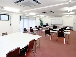 Uma sala de conferência com uma mesa comprida, várias cadeiras, um quadro branco e uma tela de projetor.
