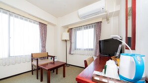 A hotel room with a wooden desk, a chair, a television, an air conditioner, and a window with curtains. - Sky Heart Hotel Koiwa (Tokyo)
