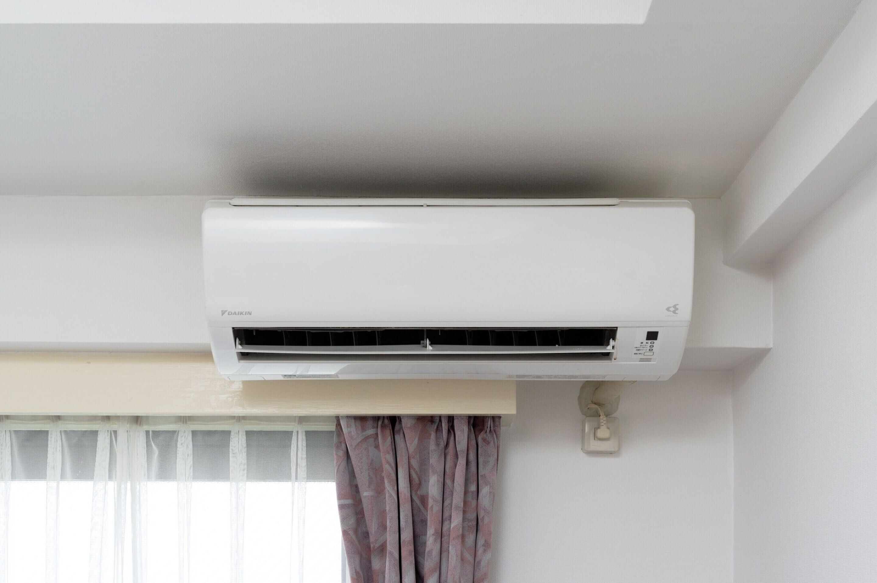 A white air conditioning unit mounted on a wall in a room with a window and curtains.