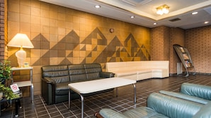 A lobby with a black leather sofa, a white sofa, a small table, a lamp, and a wall with a geometric pattern. - Sky Heart Hotel Koiwa (Tokyo)