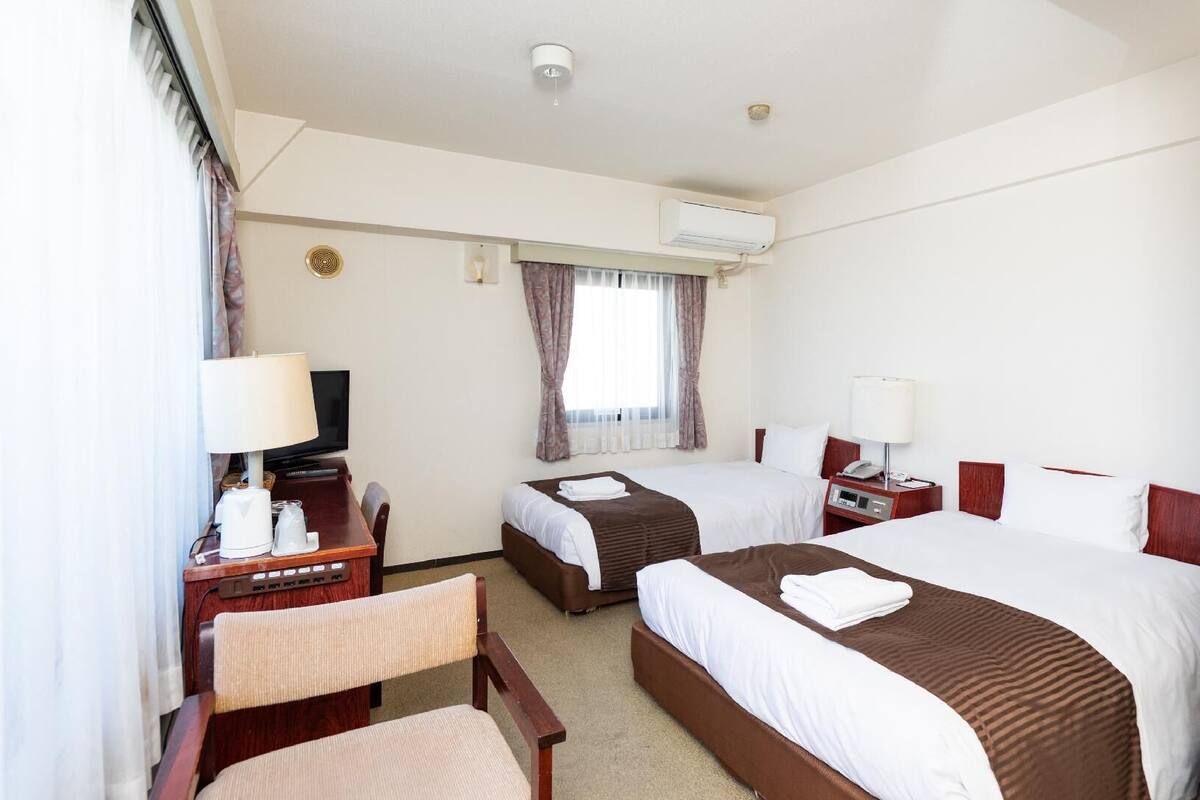 Une chambre d’hôtel avec deux lits, un bureau avec une télévision, une chaise, une table de chevet avec une lampe et un appareil de climatisation.