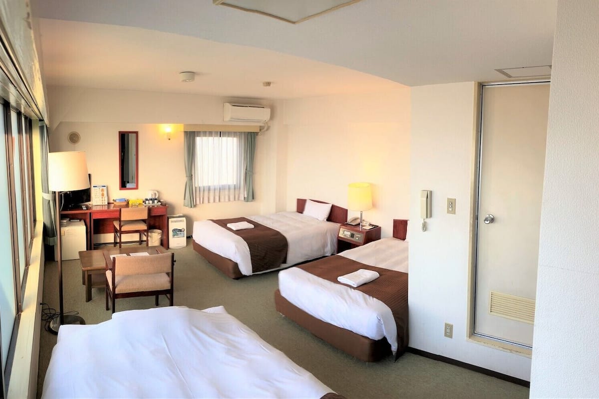 Une chambre d’hôtel avec deux lits, un bureau avec une chaise, une lampe de bureau, un téléphone et un appareil de climatisation.