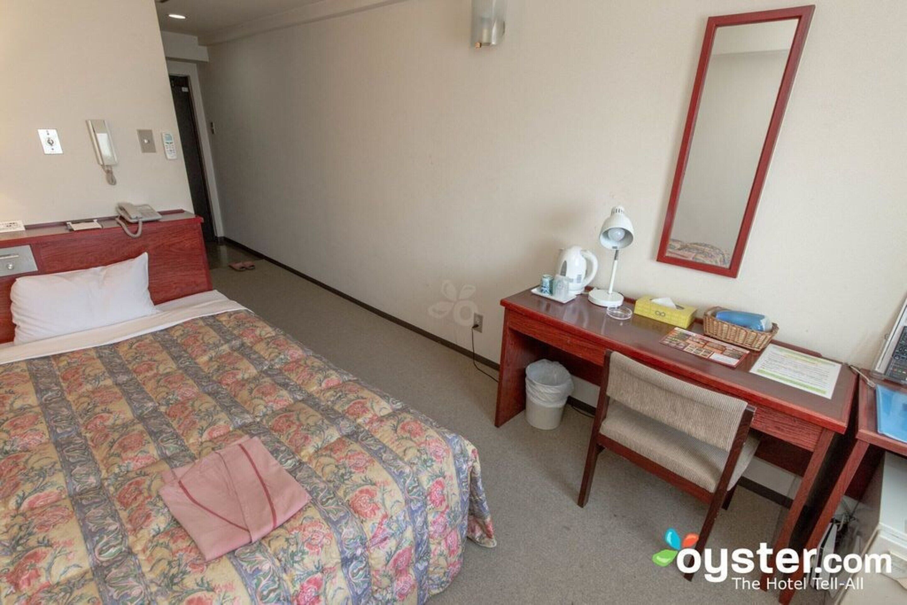 A hotel room with a bed, a desk, a chair, a mirror, a telephone, and a waste bin.