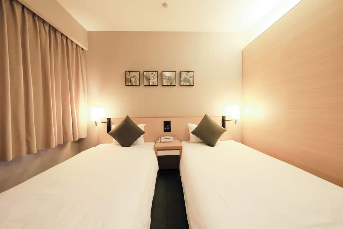A hotel room with two beds, a nightstand, a telephone, and three framed pictures on the wall.
