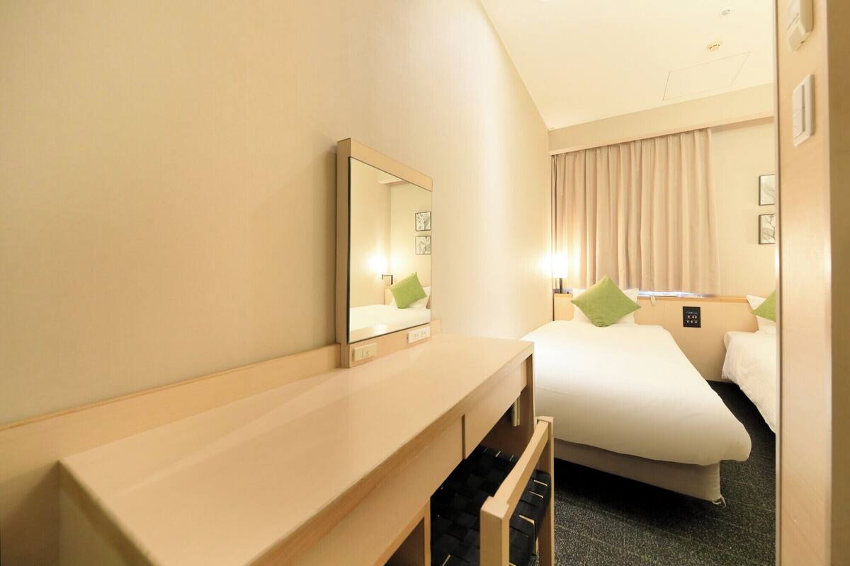 A hotel room with a bed, a bedside table, a mirror, and a window with curtains.