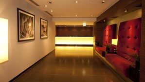 A hotel lobby with a reception desk, framed artwork on the walls, and a red upholstered seating area. - Yaesu Terminal Hotel (Tokyo)