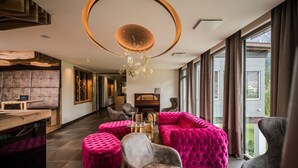Een modern interieur met een zithoek met gestoffeerde banken en poefs, een houten salontafel en een unieke ronde plafondlamp.