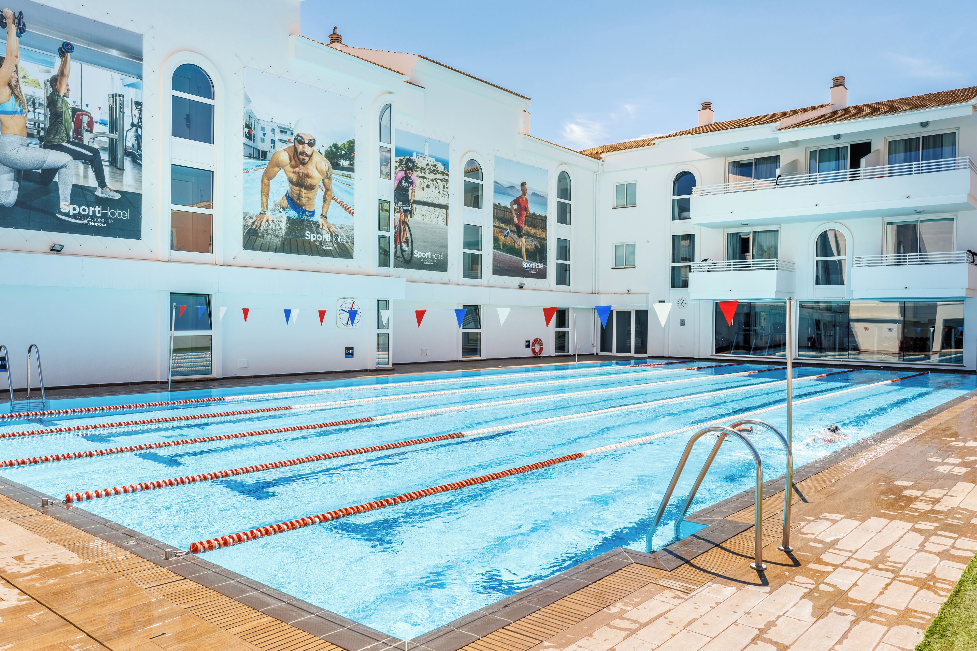 Una piscina con varias pistas de natación, un puesto de socorrista y un edificio con publicidad.