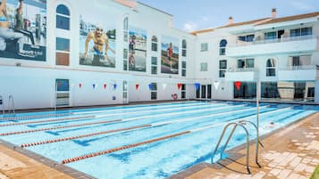 Una piscina con varias pistas de natación, un puesto de socorrista y un edificio con publicidad.